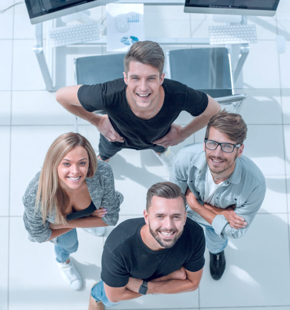 three young people stand in the office with their arms crossed and look up. One holds his hands on his belt