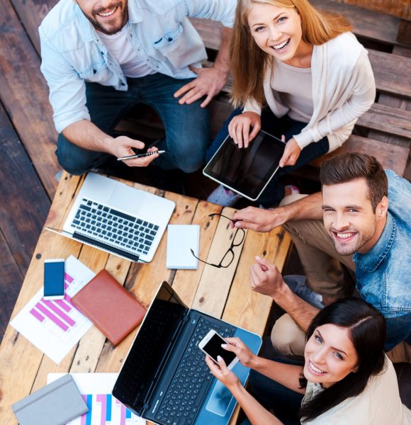 Creative team. Top view of four young people working together and looking at camera while sitting outdoors